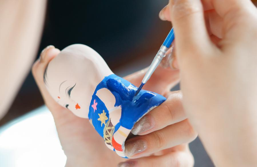 Hands painting blue clothing and decorative details on an A Fu figure