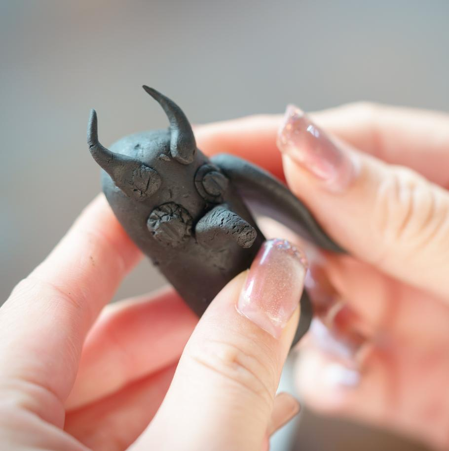 Hands shaping the details of a small dark-clay animal